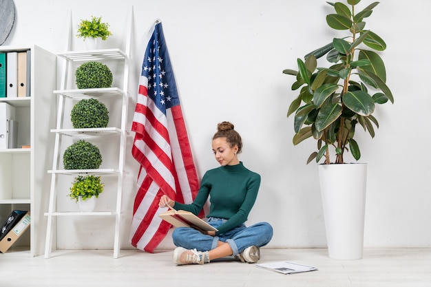 Full shot girl sitting on the floor and reading indoors