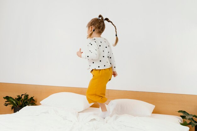 Free photo full shot girl standing on bed at home