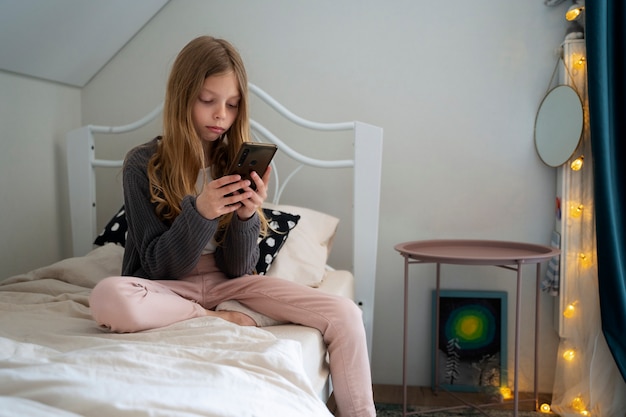 Free photo full shot girl with smartphone in bedroom