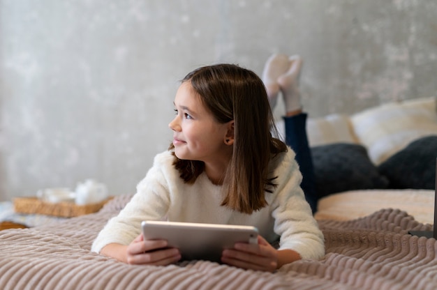 Free photo full shot girl with tablet in bed