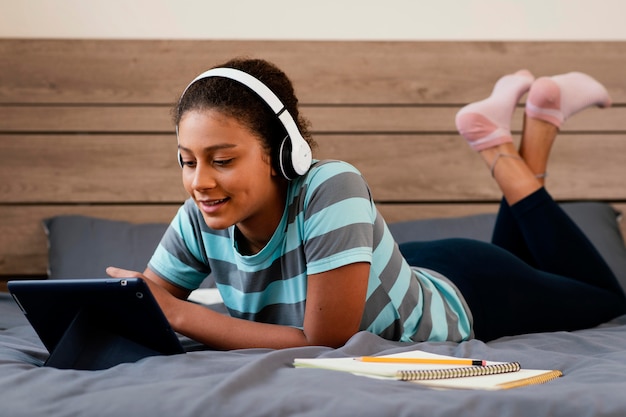 Full shot girl with tablet and headphones  in bed