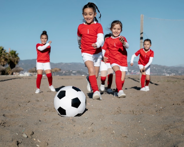 Девушки в полный рост играют в футбол на пляже