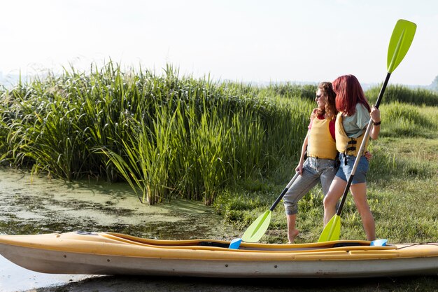 Full shot girls standing near kayak holding paddles