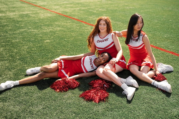 Full shot happy cheerleaders sitting on grass