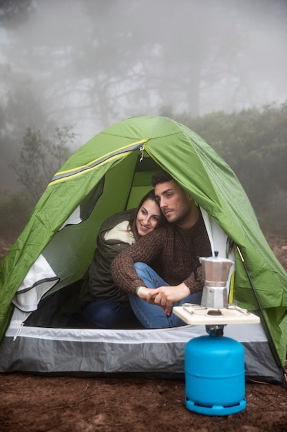 Full shot happy couple sitting in tent