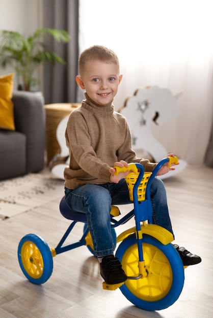 Full shot happy kid sitting on tricycle at home