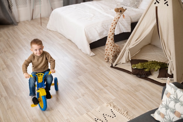 Free photo full shot happy kid sitting on tricycle indoors