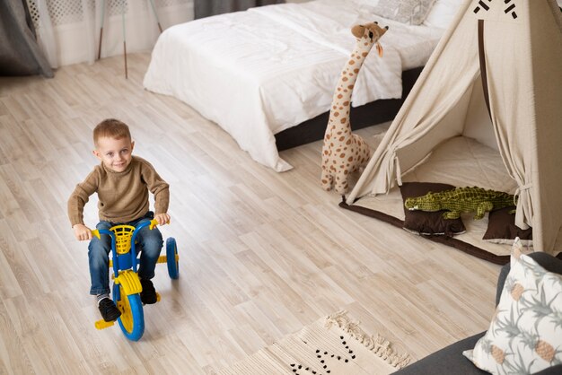 Full shot happy kid sitting on tricycle indoors