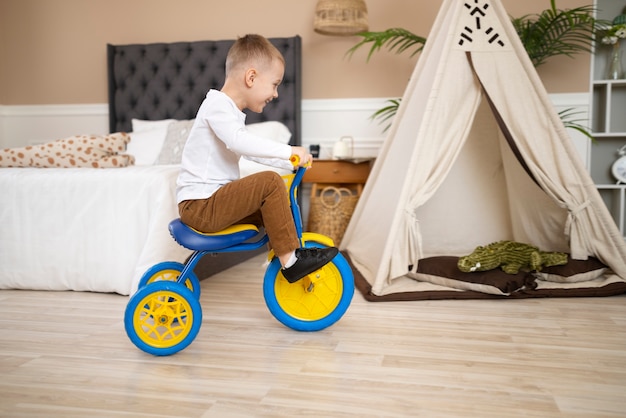 Full shot happy kid with tricycle indoors