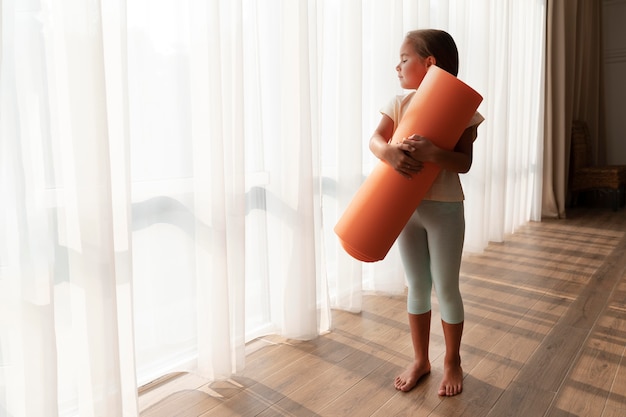 Полноценный ребенок, держащий коврик для йоги