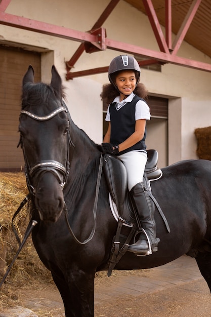 Бесплатное фото Полный кадр ребенок учится кататься на лошади
