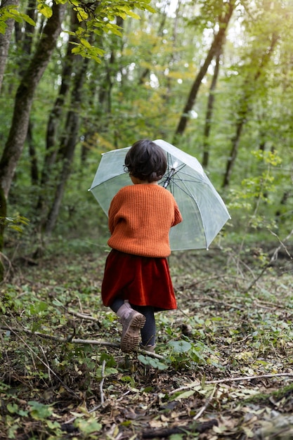 Full shot kid in nature with umbrella