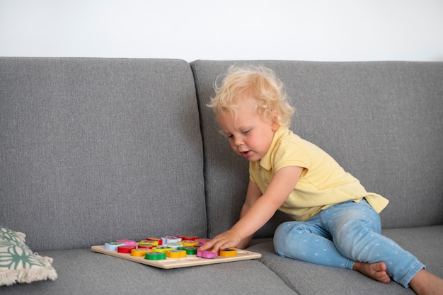 Full shot kid playing on couch with puzzle