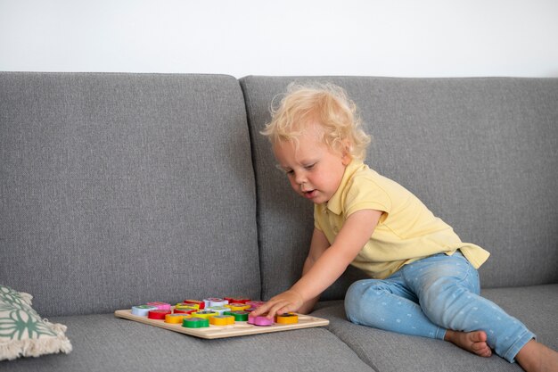 Full shot kid playing on couch with puzzle