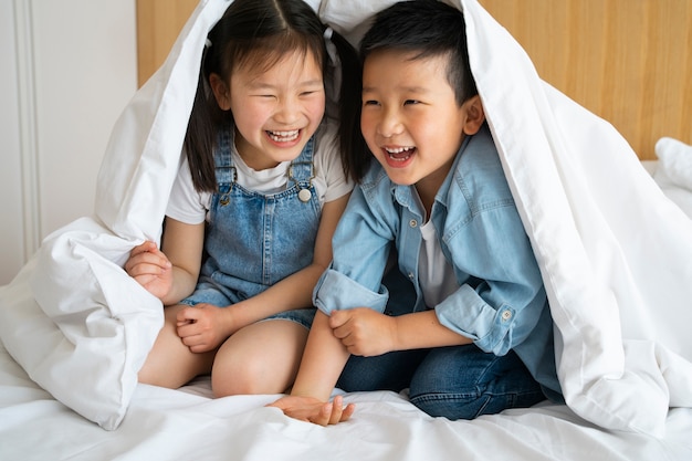 Free photo full shot kids sitting under blanket