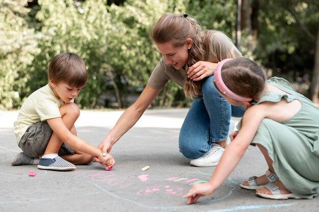 Full shot kids and teacher drawing on ground