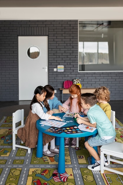 Full shot kids and teacher sitting at table