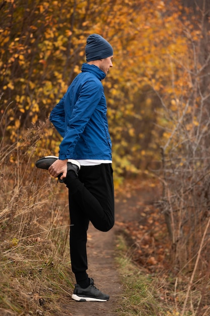 Free photo full shot male stretchig his legs in forest