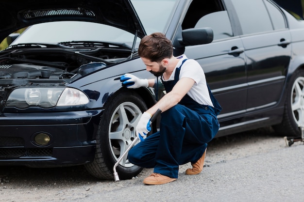 Full shot of man crouched next to car