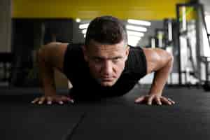 Free photo full shot man doing push-ups at gym