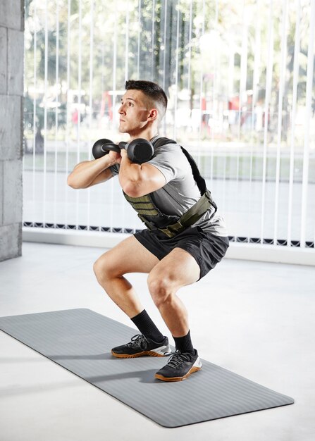 Full shot man doing squats with dumbbell