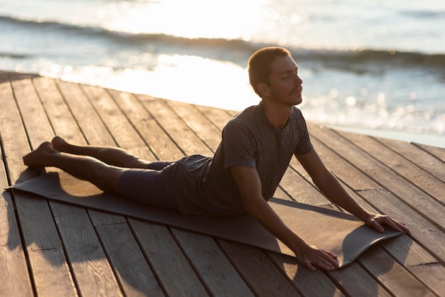 Full shot man doing upward facing dog on mat outside