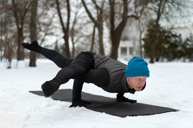 Foto gratuita uomo a tutto campo che fa yoga quando fa freddo