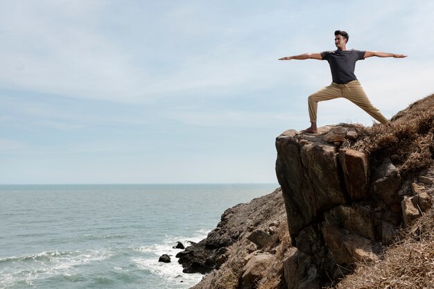 Full shot man doing yoga on rocks