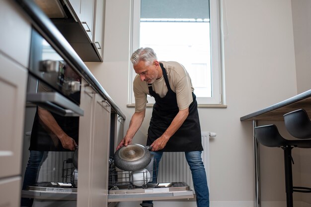 Мужчина в полный рост загружает посудомоечную машину