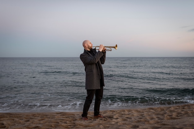 Full shot man playing trumpet at seaside
