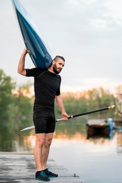 Full shot man posing with oar and canoe