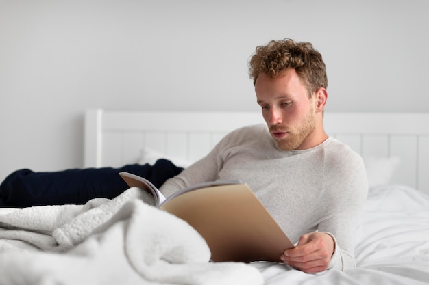 Free photo full shot man reading book in bed