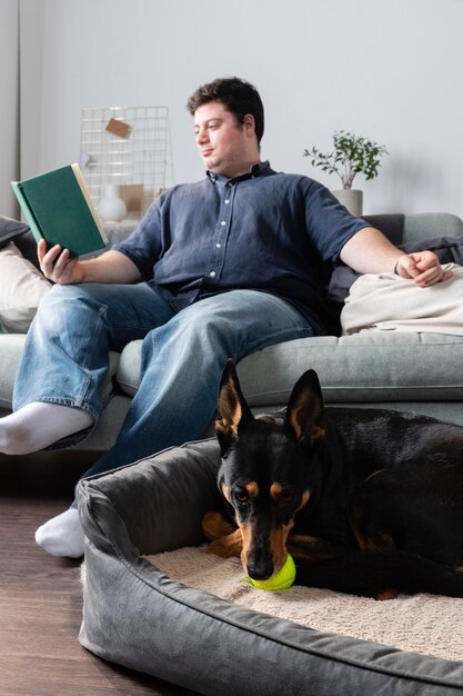 Full shot man reading with cute dog indoors