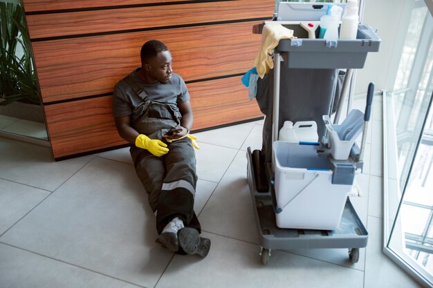 Full shot man sitting near cleaning cart