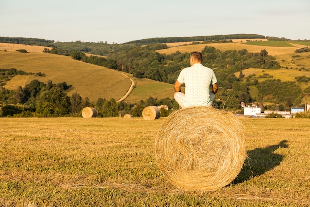 Full shot man sitting on roll of hays