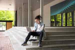 Free photo full shot man sitting on stairs with laptop