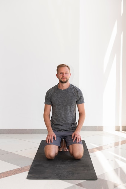 Full shot man sitting on yoga mat