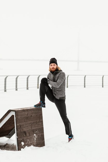 Full shot man in snow stretching