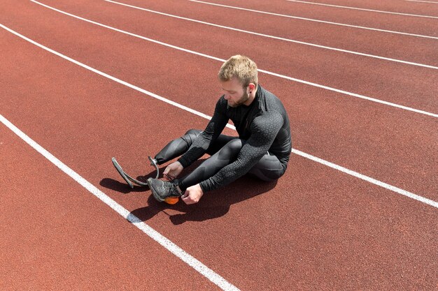 ランニングトラックで靴紐を結ぶフルショットの男