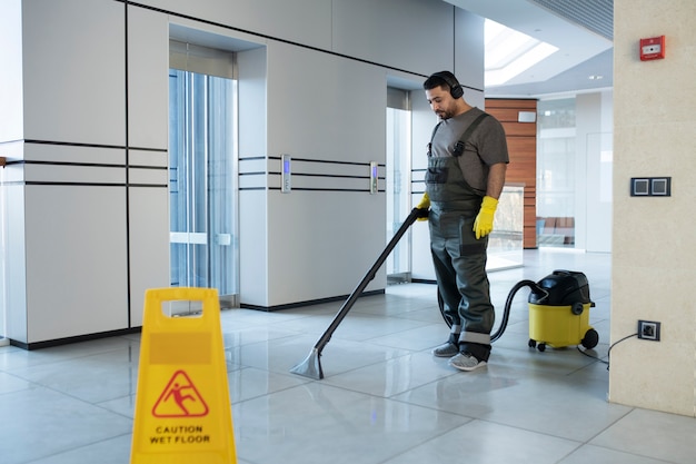 フルショットの男が床を掃除機で掃除する