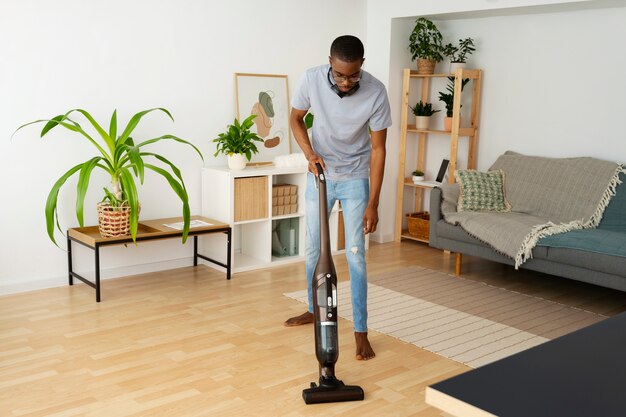 フルショットの男が床を掃除機で掃除する