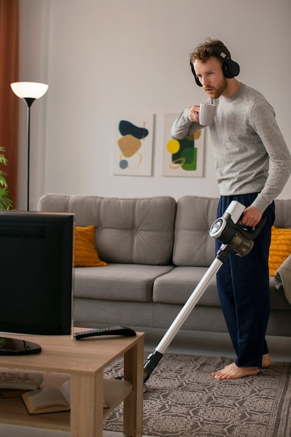 Full shot man vacuuming and watching tv