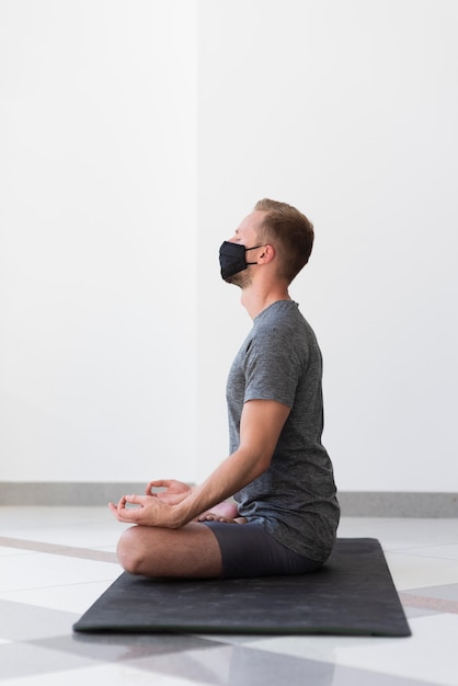 Полный снимок человека с маской, практикующего позу йоги