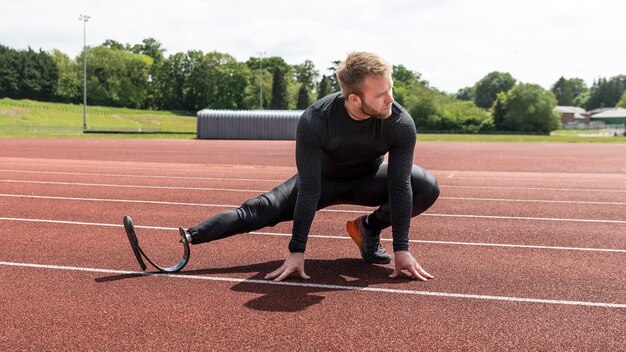 Full shot man with prosthetic leg stretching on running track