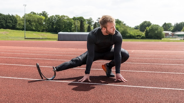 Full shot man with prosthetic leg stretching on running track