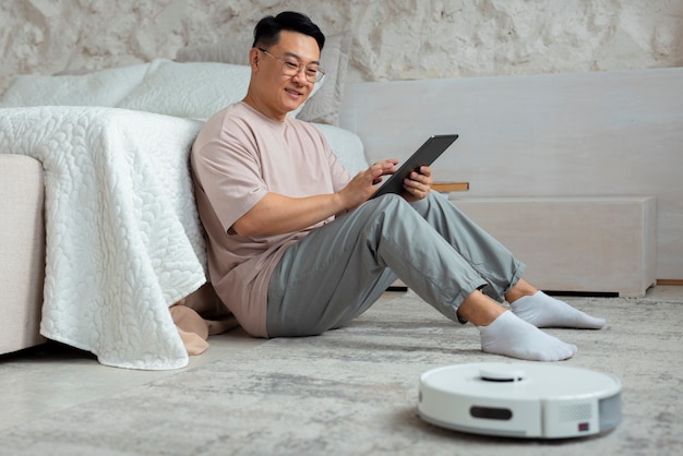 Full shot man with robotic vacuum cleaner at home