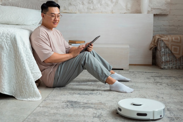 Full shot man with robotic vacuum cleaner at home