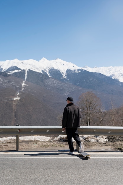 Foto gratuita uomo a tutto campo con skateboard a guardare le montagne