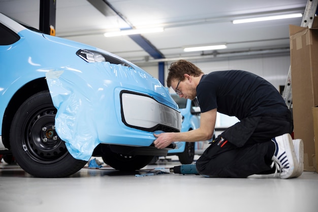 Full shot man wrapping car with blue cover