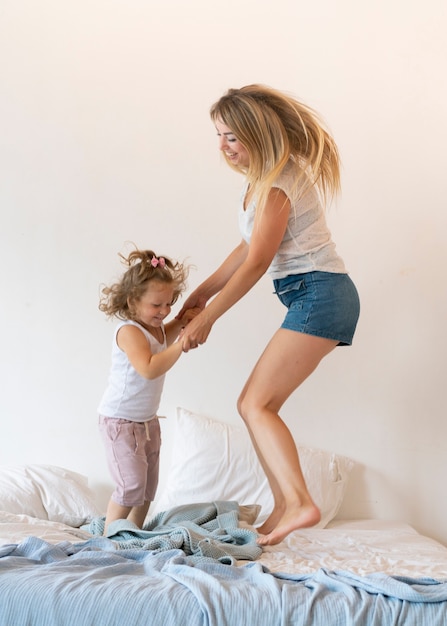 Free photo full shot mother and daughter jumping in bed